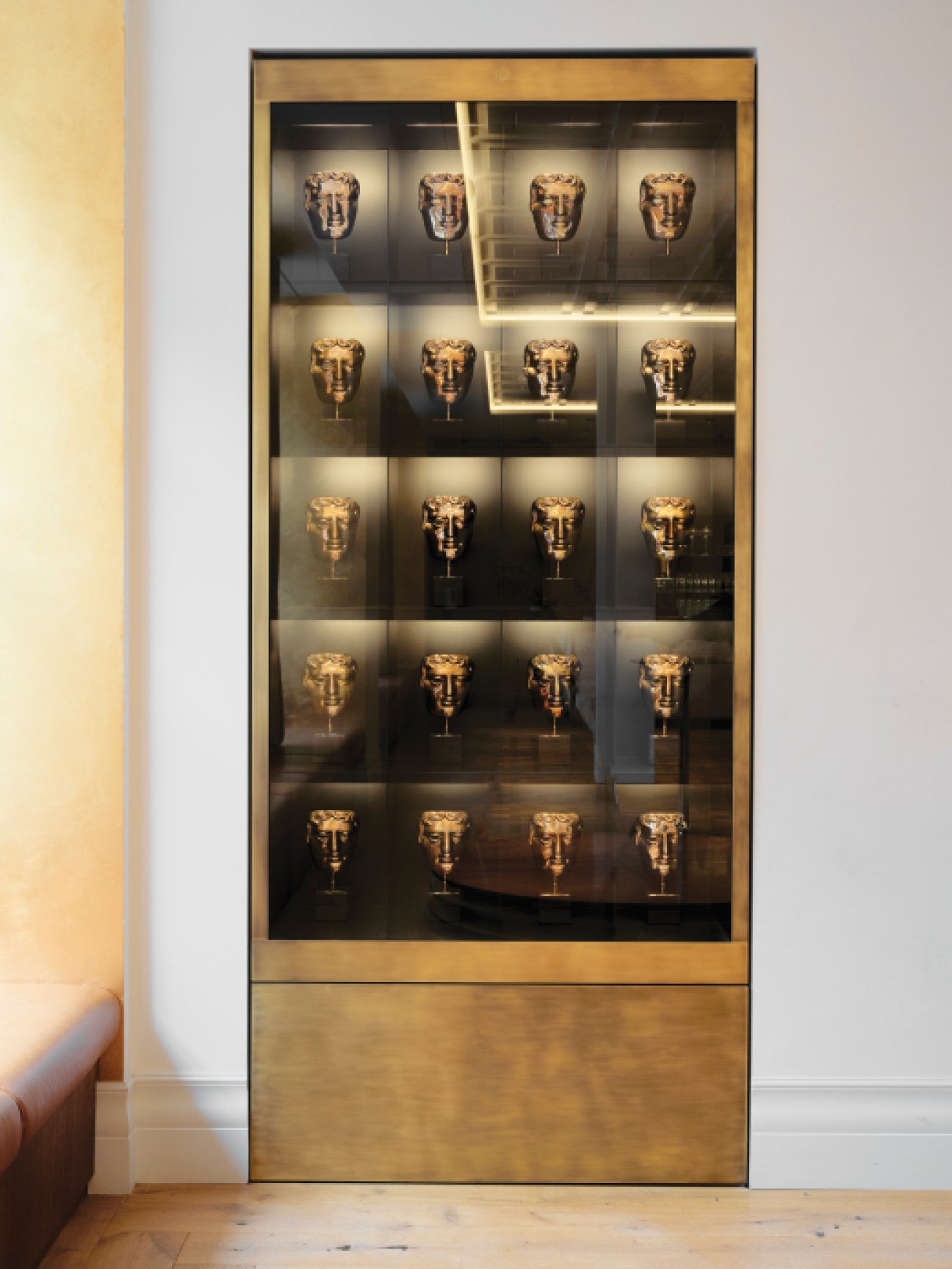 Glass display cabinet with five rows of golden BAFTA award masks arranged on illuminated shelves