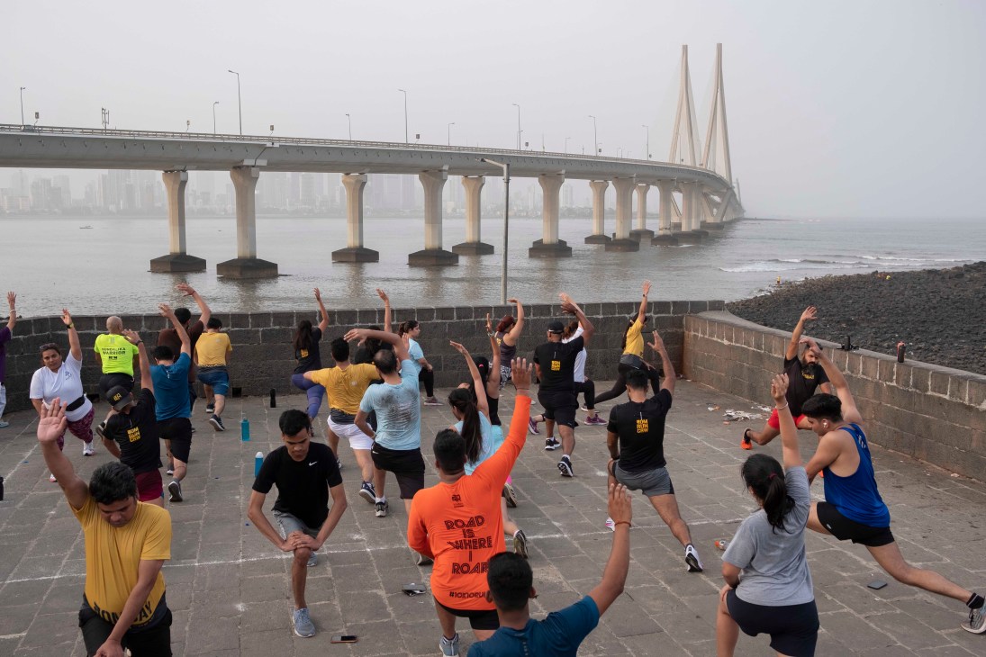 Group of people doing stretching exercises on a waterfront promenade with a large cable-stayed bridge in the background
