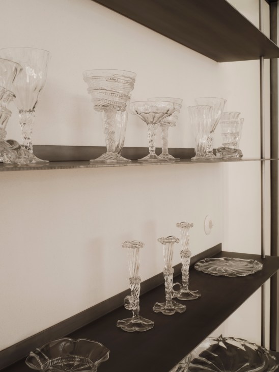 Collection of clear crystal glassware including goblets, bowls and stemware displayed on dark shelves