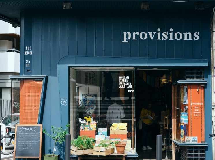 Blue storefront of Provisions specialty food store with decorative balcony and street display