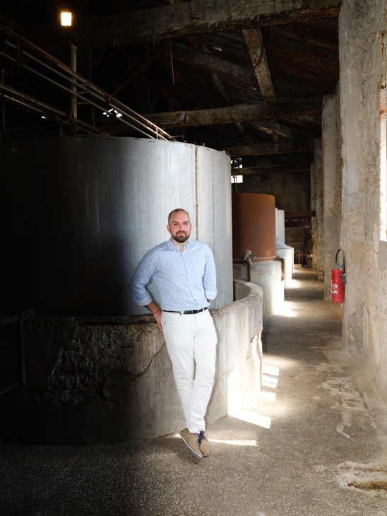 Raphael Seghin stands in an industrial space with large metal tanks and concrete walls.