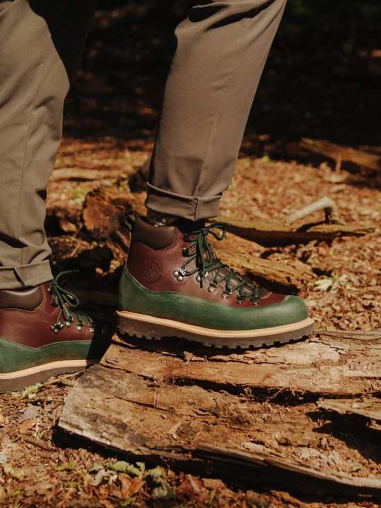 Person wearing brown and green hiking boots walking on fallen logs in autumn forest terrain