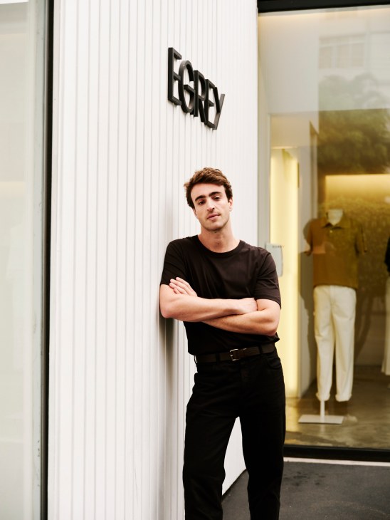Egrey founder Eduardo Toldi standing with arms crossed wearing black clothing in front of white storefront