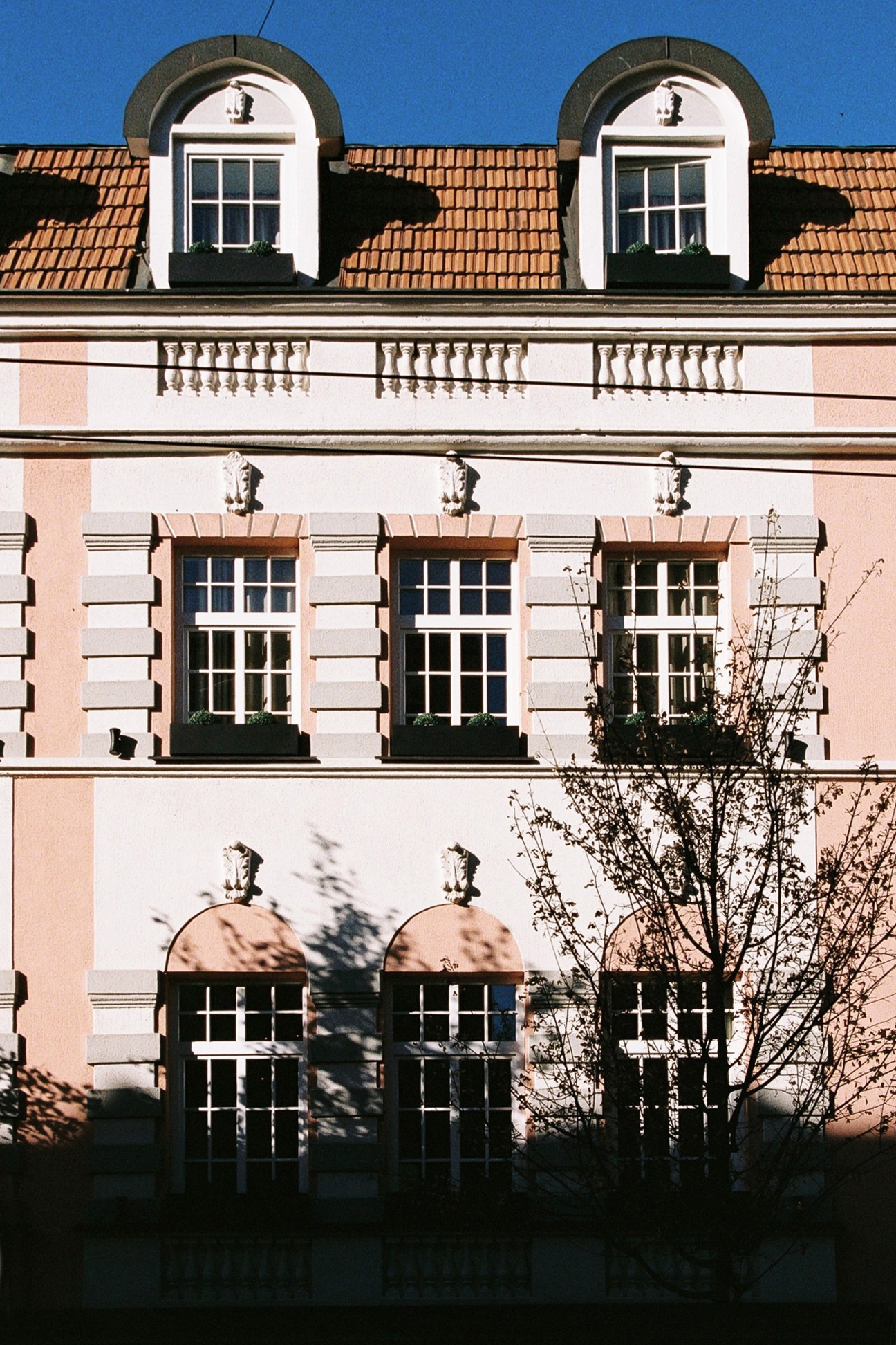 Historic building facade with pink and white exterior, arched windows and terracotta roof tiles under blue sky.