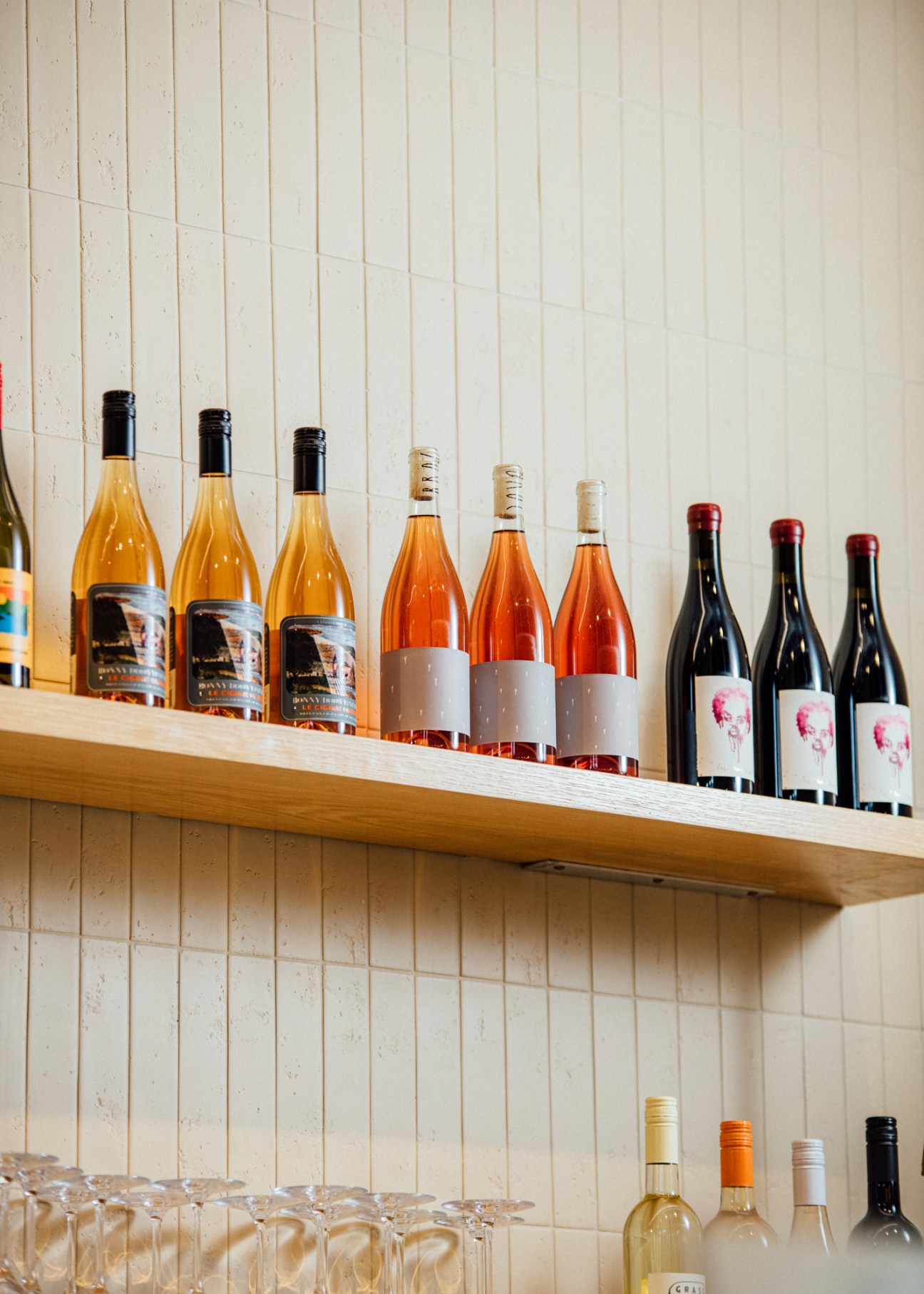 Wine bottles arranged on wooden shelf displaying orange, rosé and red wines with various labels
