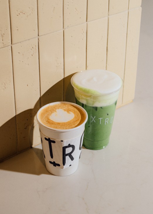 Two beverages in takeaway cups - a latte with heart-shaped foam art and a green matcha drink with white foam topping
