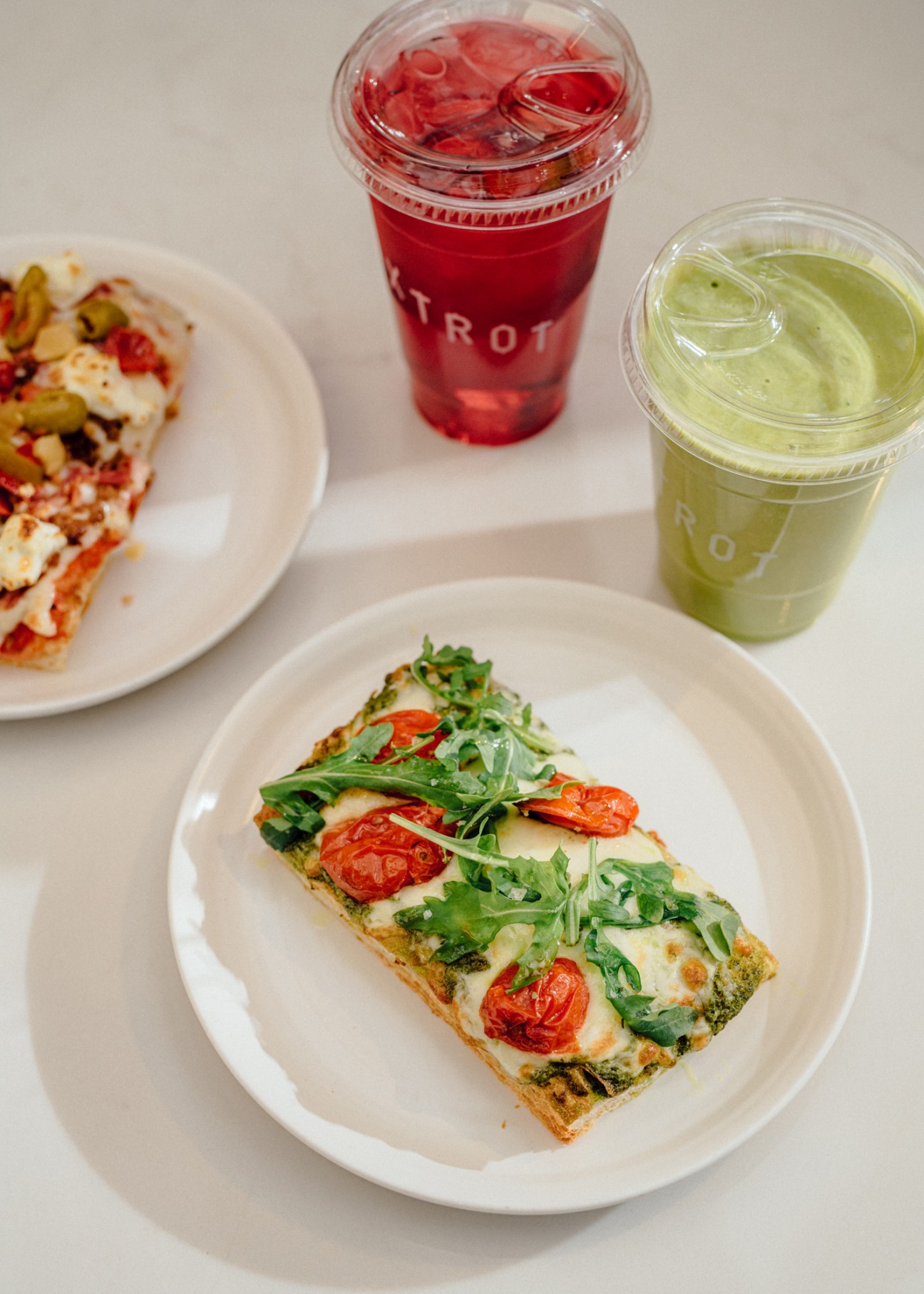 Flatbread topped with cherry tomatoes, greens and cheese on white plate with beverages in background
