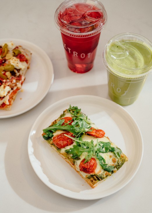 Flatbread topped with cherry tomatoes, greens and cheese on white plate with beverages in background
