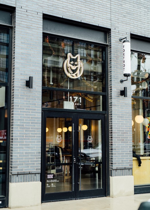 Modern storefront with glass windows, black frames, and illuminated fox logo sign on brick building