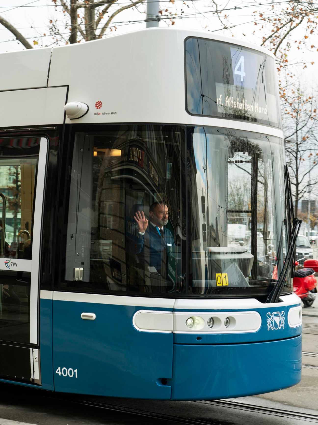 A Zürich Flexity tram in blue and white livery with a conductor waving from the window.
