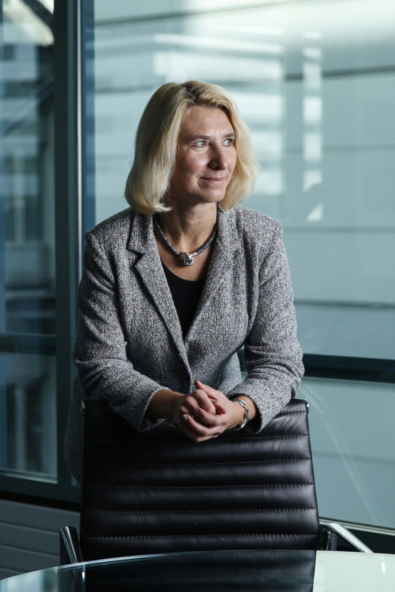 Professional woman in gray blazer sitting at conference table in modern office with glass windows