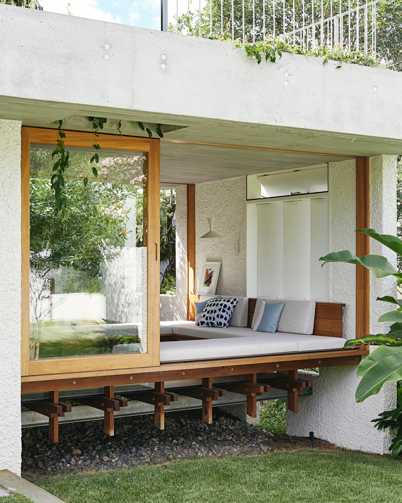Modern outdoor seating area with wooden frame structure elevated on posts beneath concrete overhang