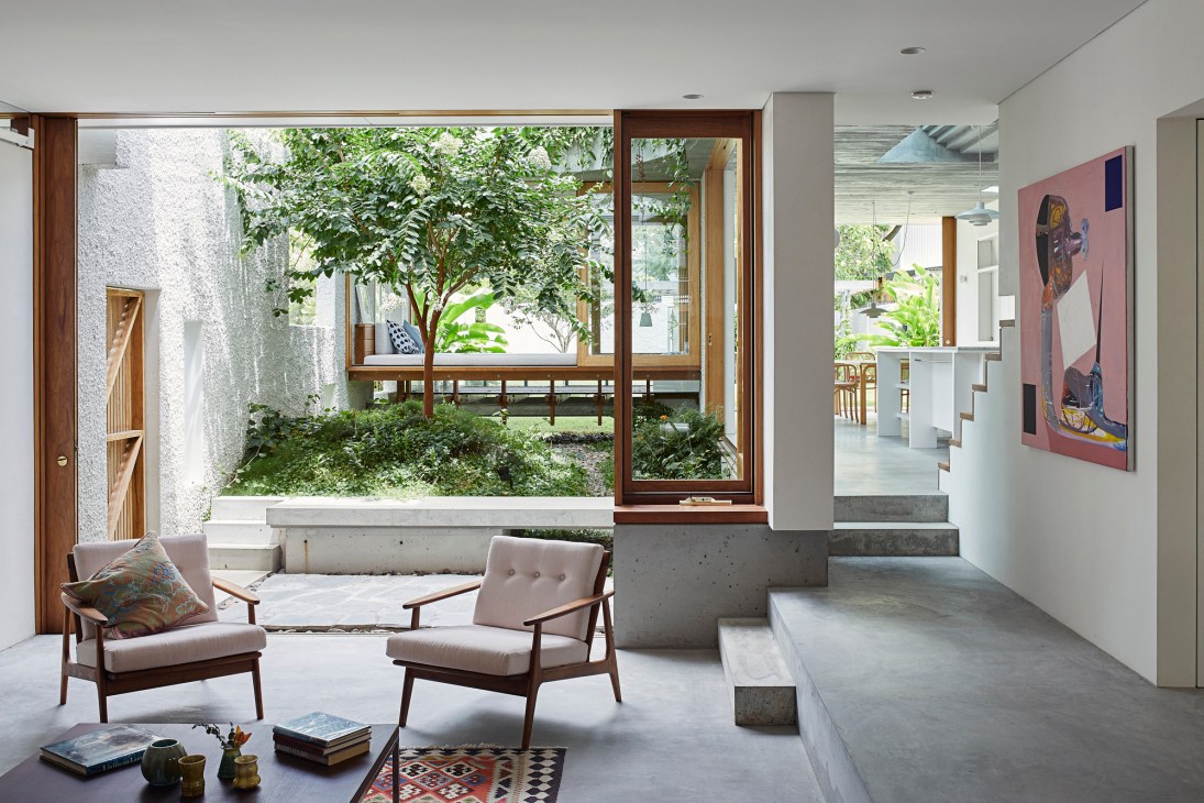 Modern living room with concrete steps, mid-century chairs, and large windows overlooking an interior courtyard garden