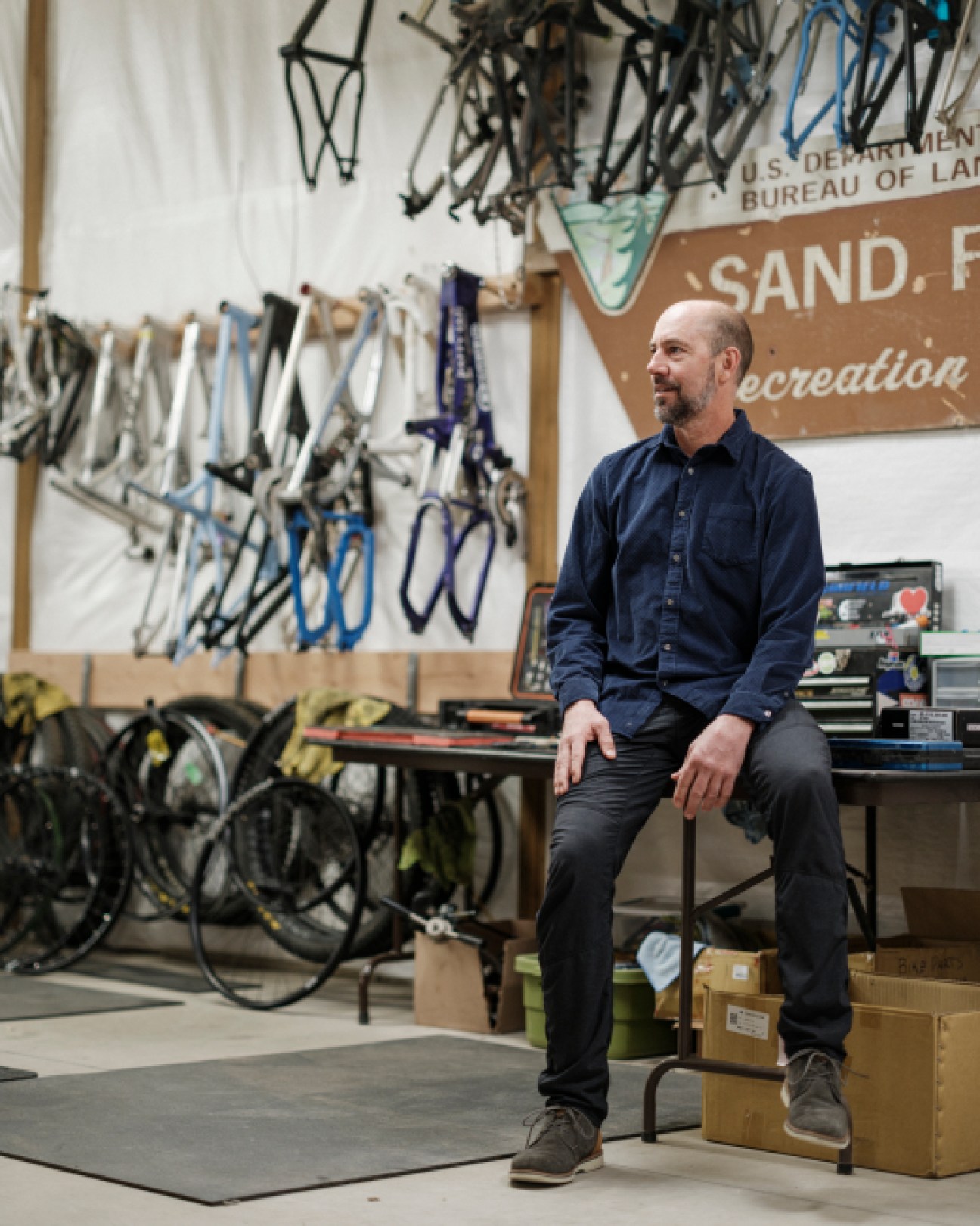 Lance Canfield sitting in his bike workshop surrounded by bicycle frames and equipment