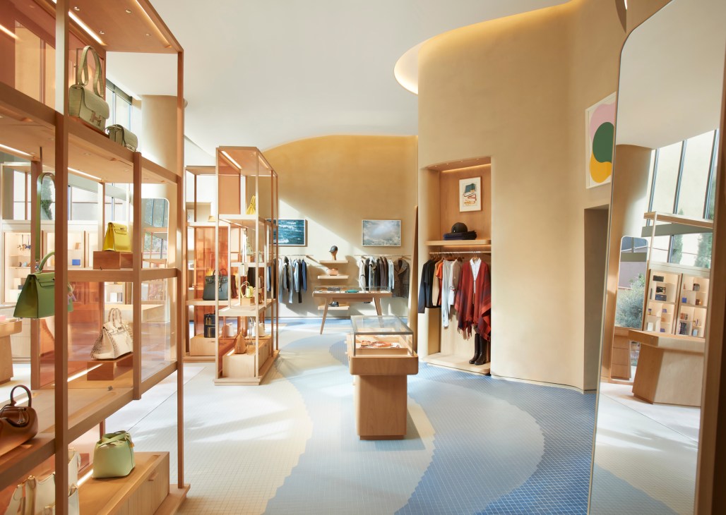 Hermès Barcelona store interior with curved walls, wooden shelving displays, and clothing racks