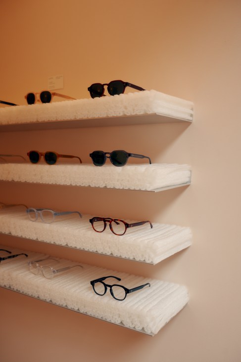 Display shelves with white textured surfaces holding various eyeglasses and sunglasses frames