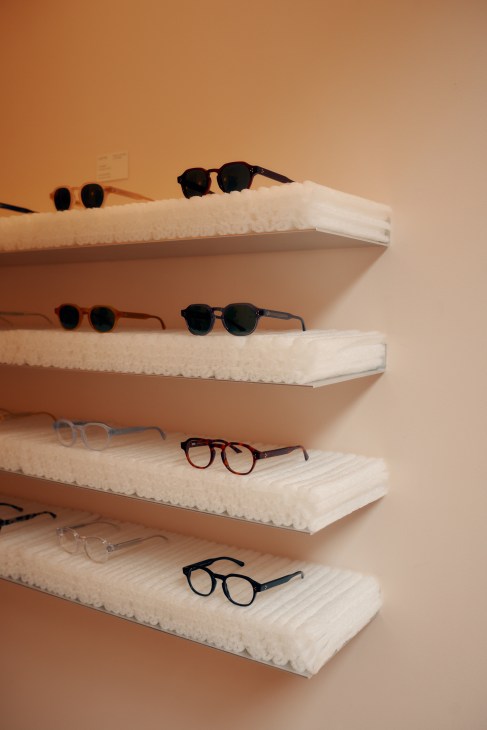 Display shelves with white textured surfaces holding various eyeglasses and sunglasses frames