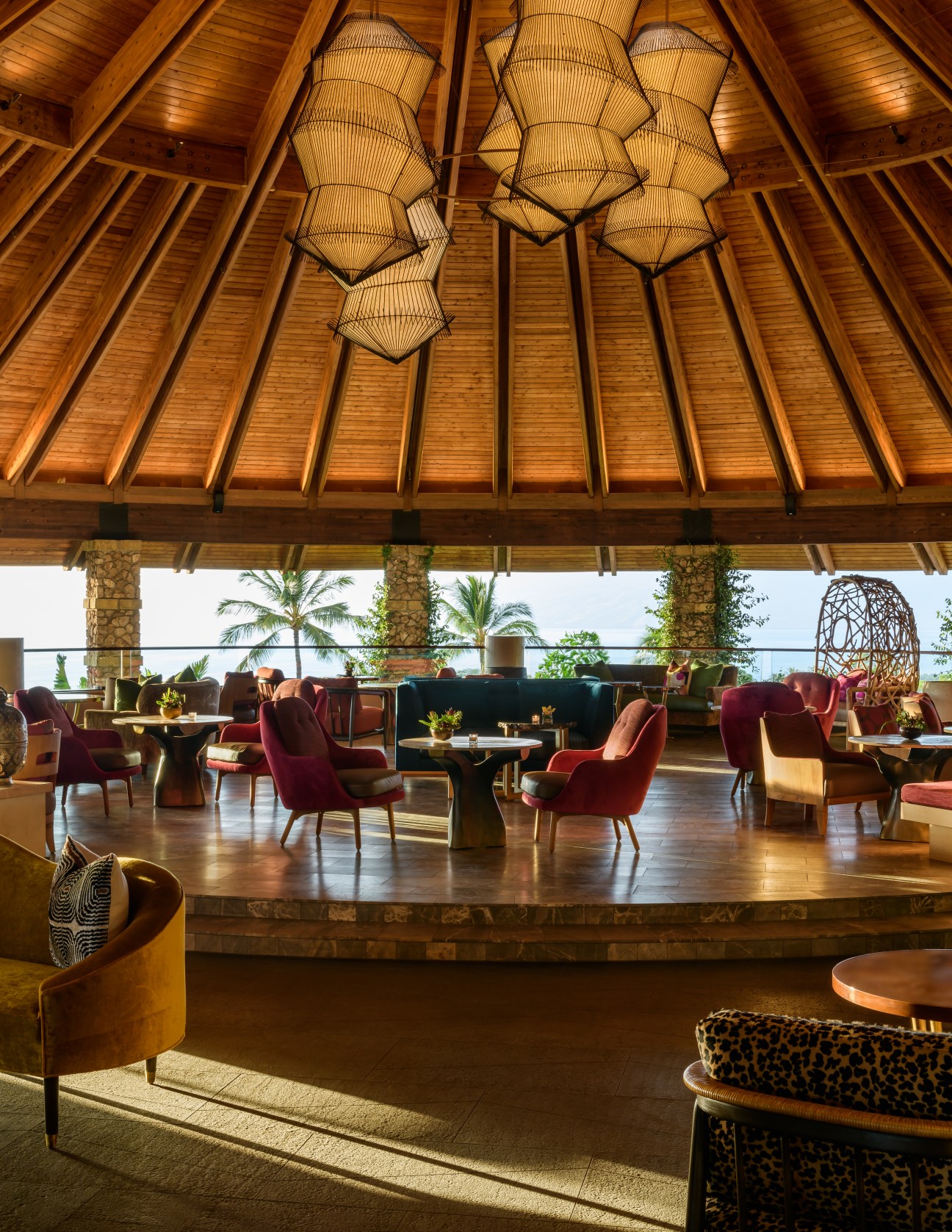 Open-air hotel lobby bar with wooden ceiling beams, wicker pendant lights, and tropical seating areas