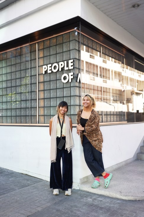 Curator Mia Tongpan standing with another person in the theatre spacestanding and smiling outside the People of Ari theatre space in Bangkok