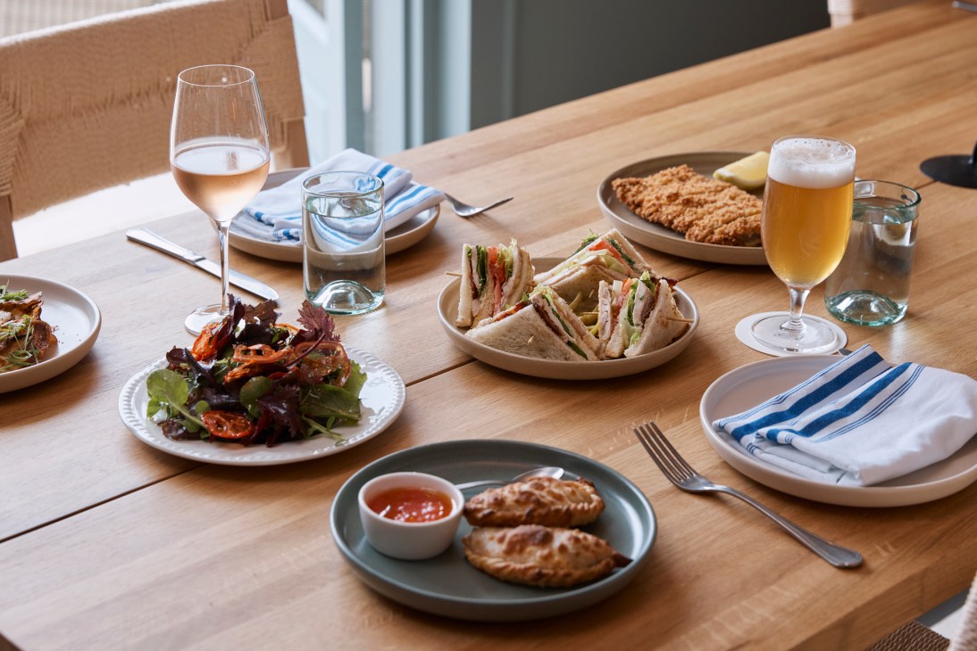 Various dishes and drinks spread across a wooden dining table with plates, glasses, and cutlery