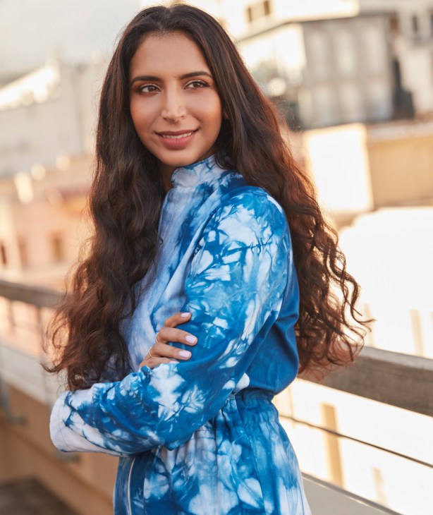 Woman in blue tie-dye shirt smiling at camera on rooftop
