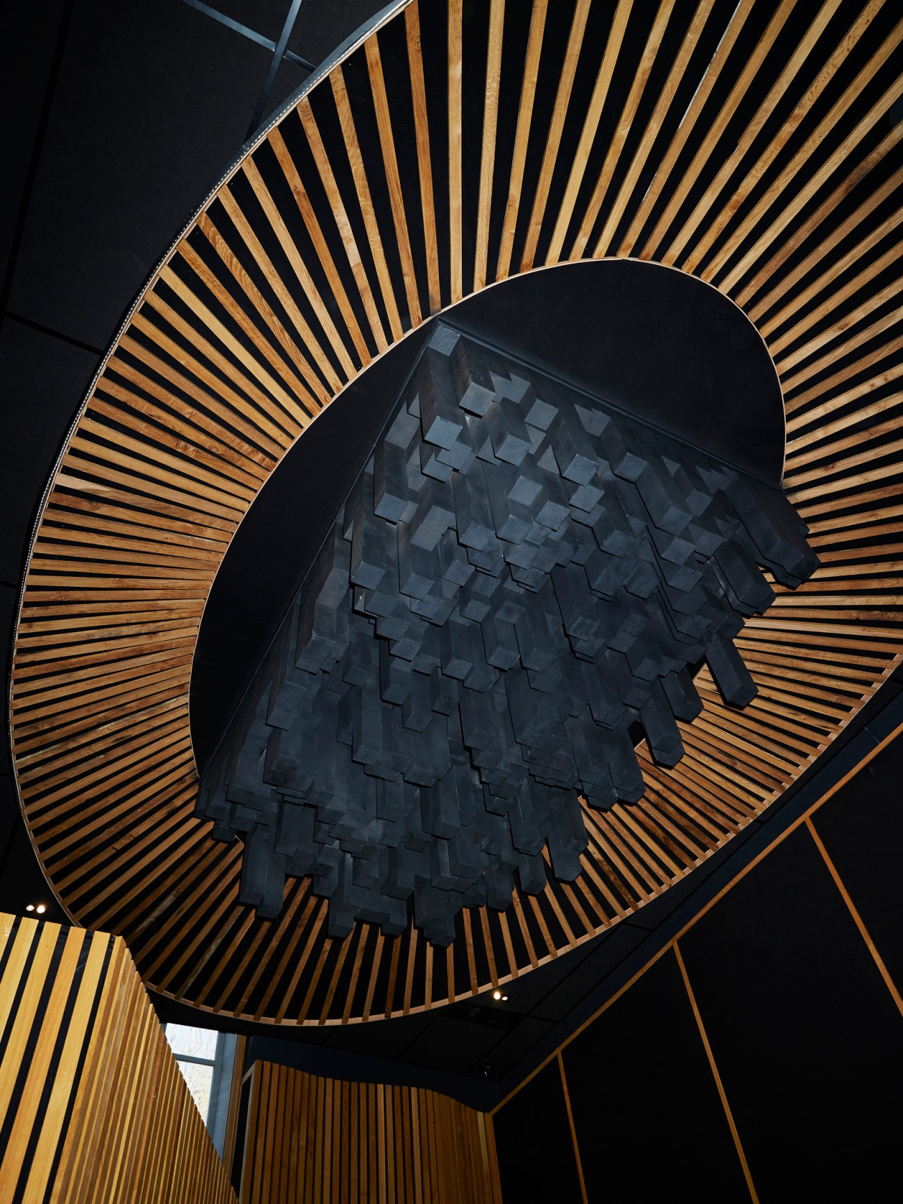Overhead view of a geometric acoustic diffuser with dark textured center panel surrounded by radiating wooden slats.