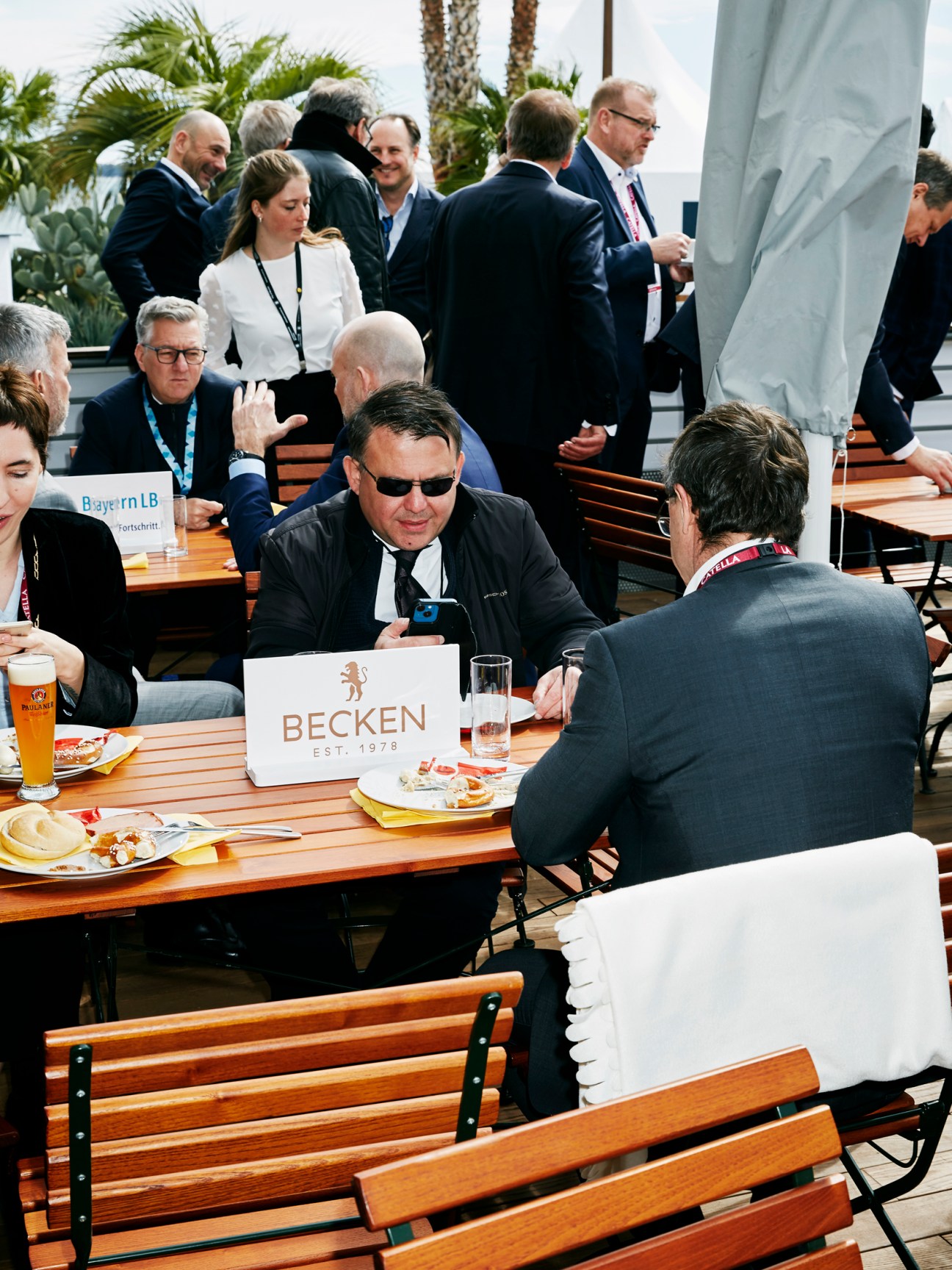 Business professionals in suits networking at outdoor tables during Mipim trade fair with palm trees in background
