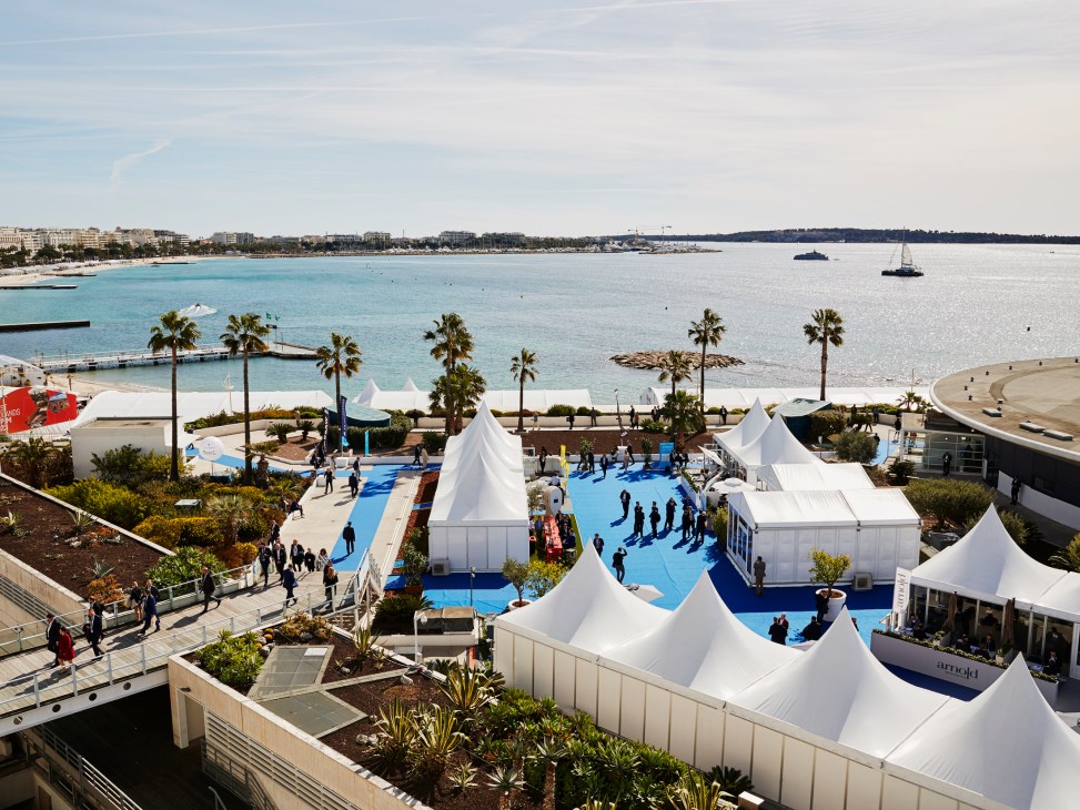 Aerial view of white exhibition tents and crowds at the Palais des Festivals et des Congrès in Cannes with bay in background