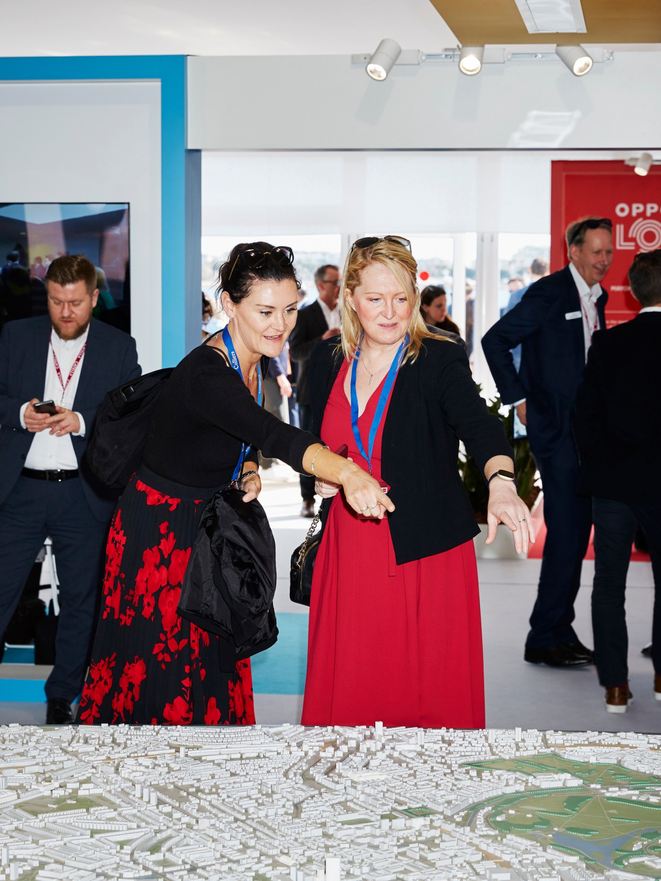 Two women examining a large white architectural scale model of London cityscape at Mipim trade fair exhibition