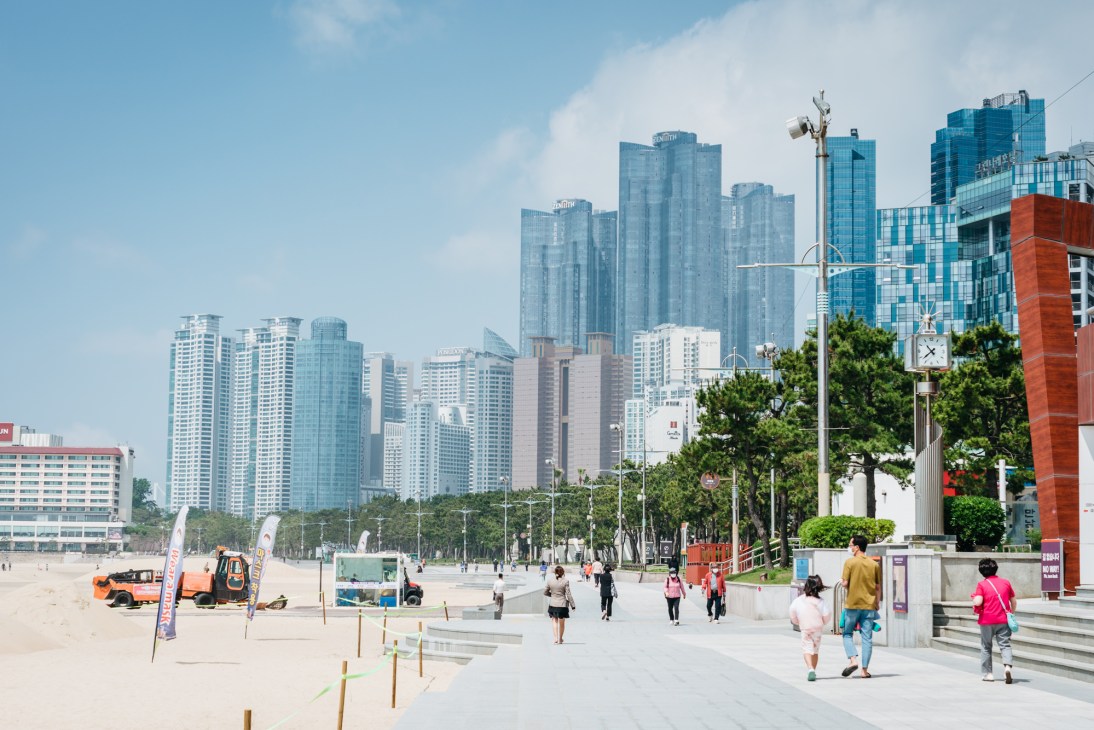 Busan beach with high-rise buildings in background and people walking on waterfront promenade