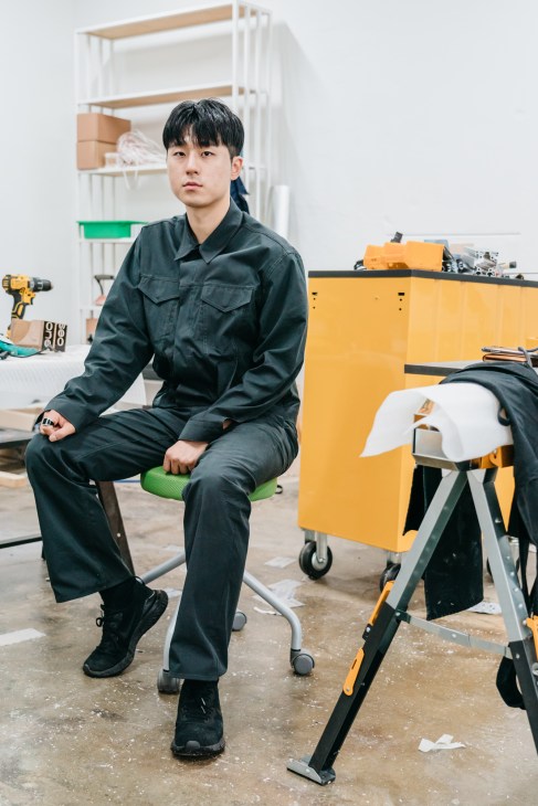 Oneseo Choi sits in his studio surrounded by yellow and white furniture pieces made from repurposed aluminum rods.