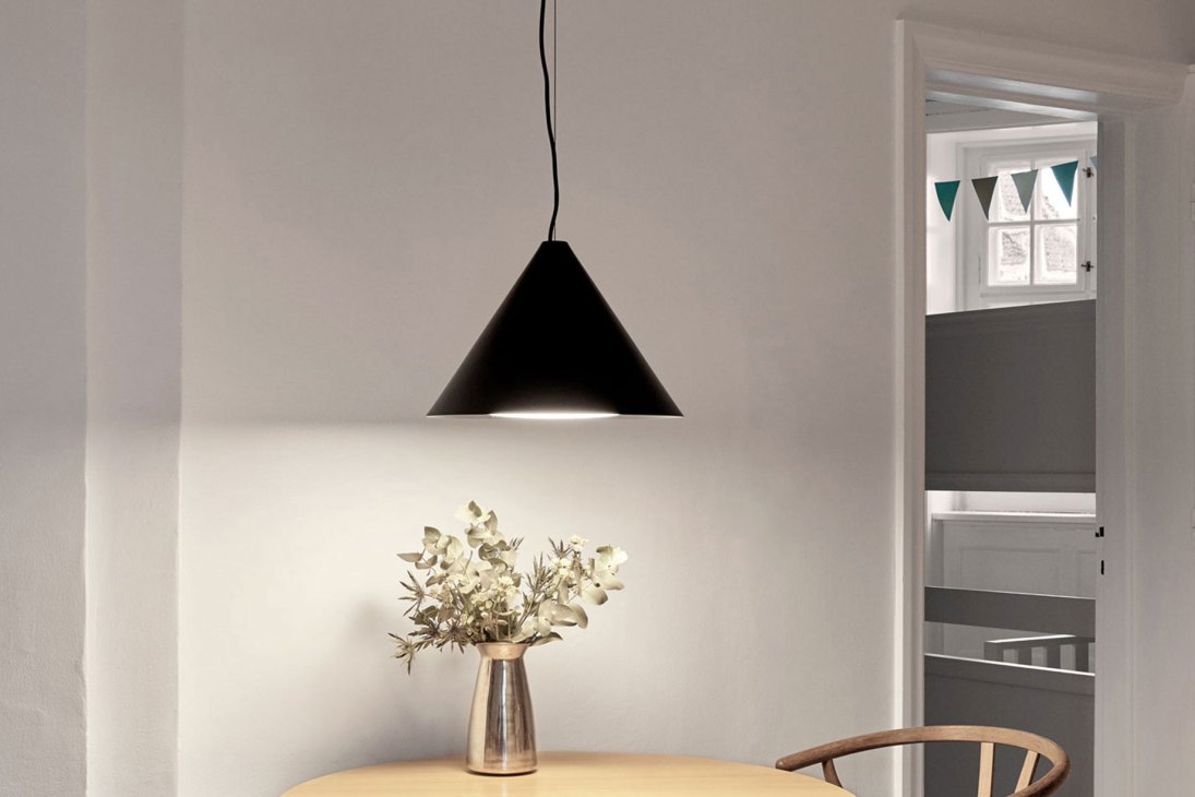 Black triangular pendant lamp hanging above dining table with vase of dried flowers and wooden chair
