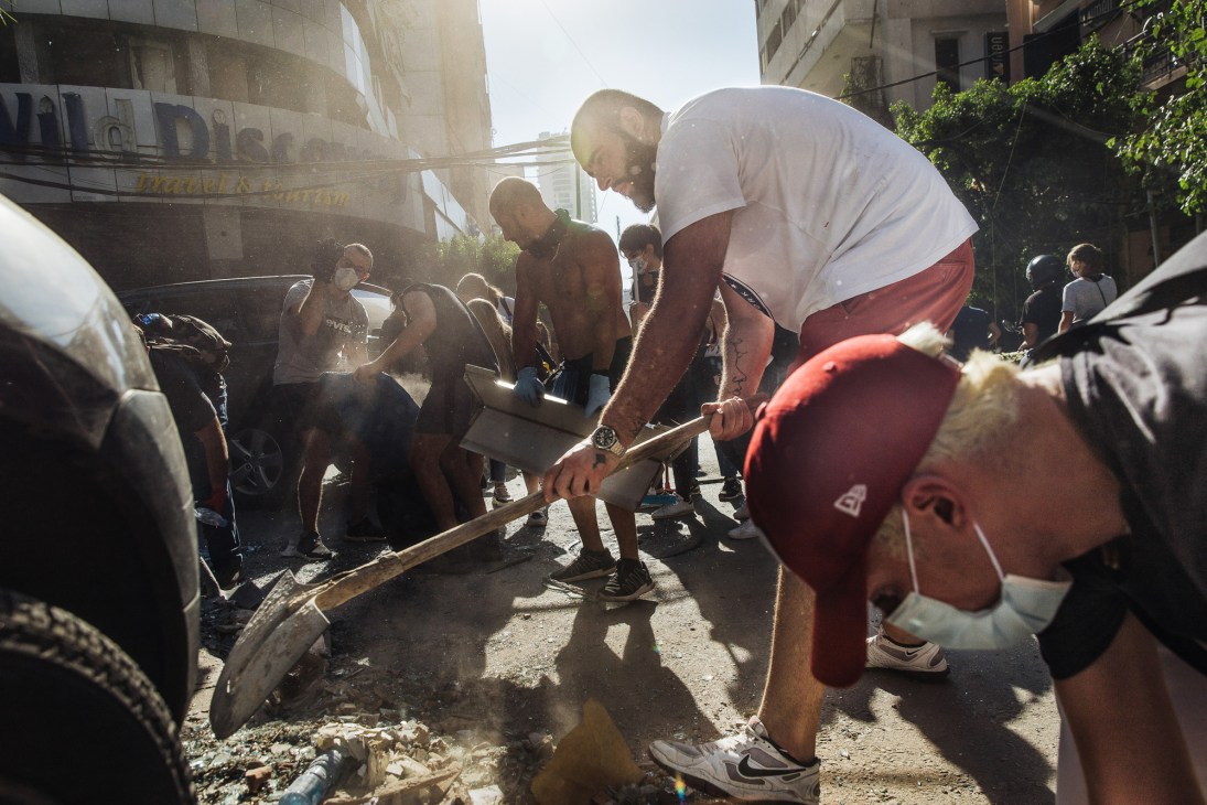 Groups of volunteers with brooms and cleaning equipment working to clear debris and glass from damaged streets