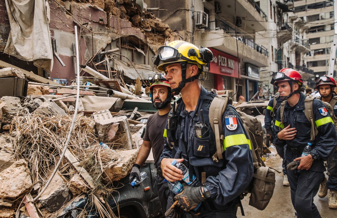 French civil defence crew in protective gear and helmets searching through rubble and debris in damaged Gemmayze district