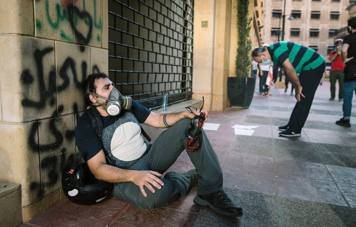 Protester wearing gas mask and protective gear sitting against wall during Beirut demonstrations