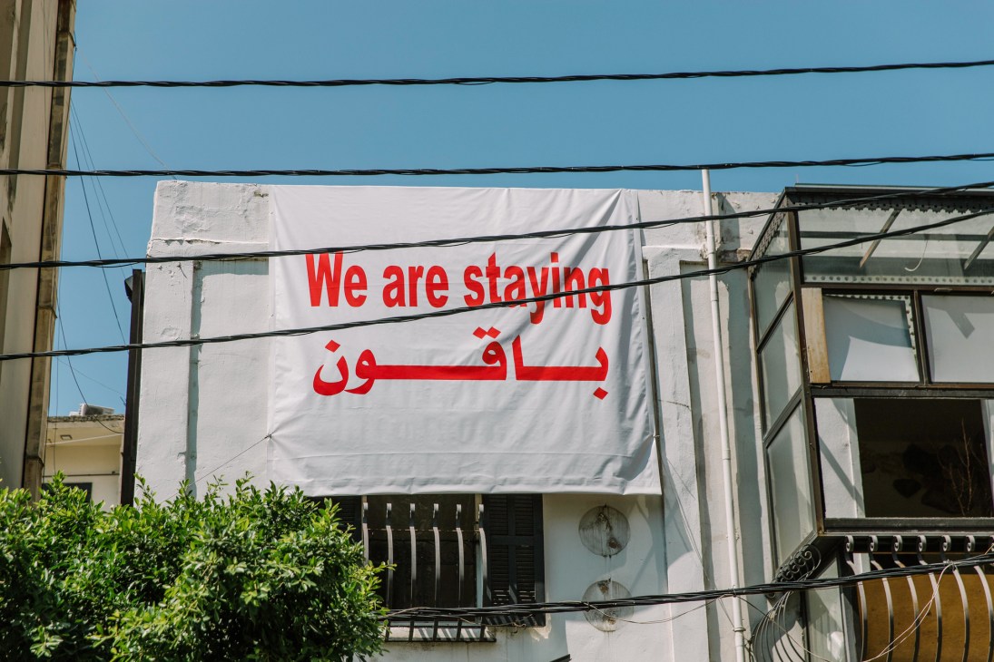 White banner with red Arabic and English text reading 'We are staying' hanging on a building