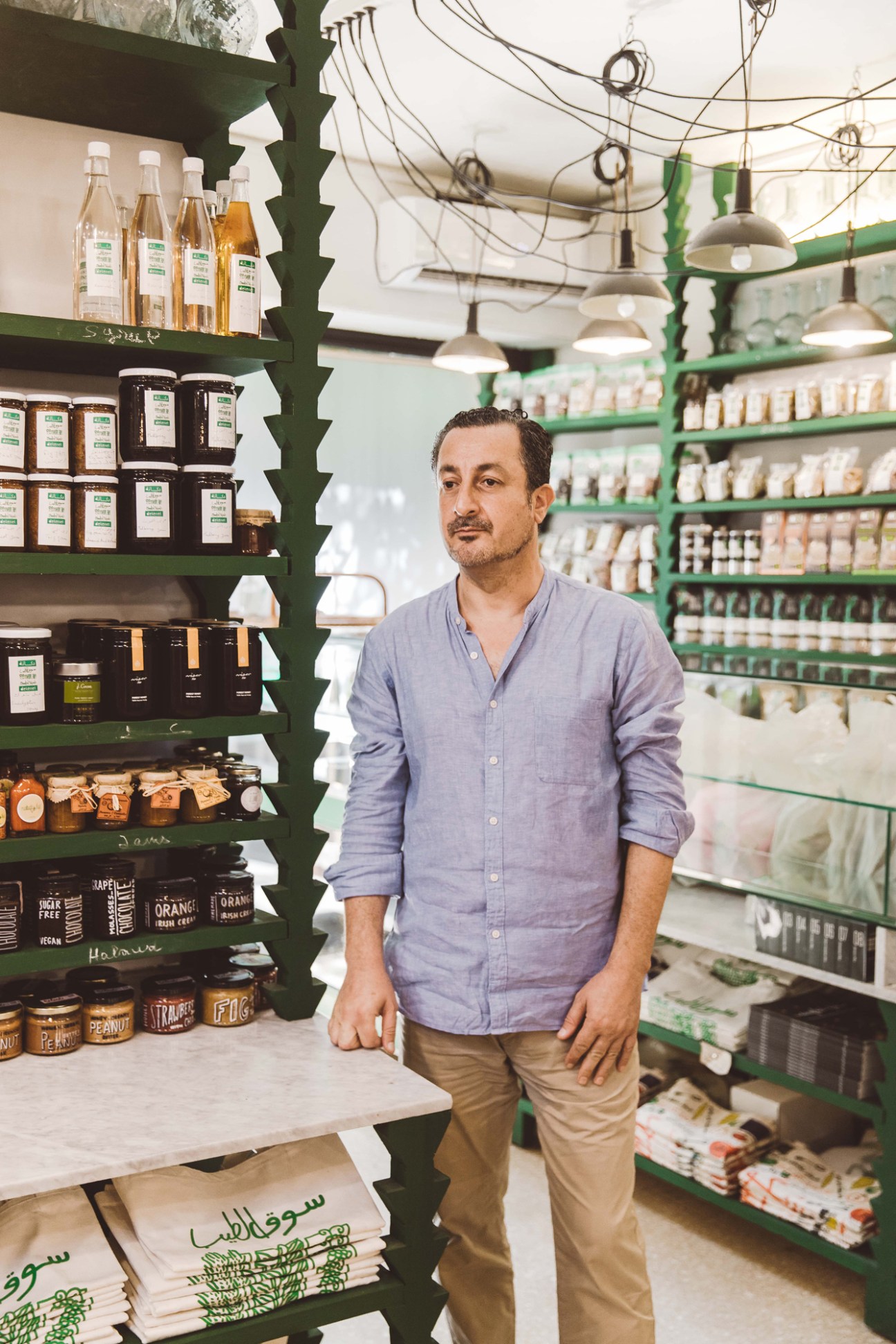 Food campaigner Kamal Mouzawak standing in a grocery store with green shelves stocked with organic products and bottles