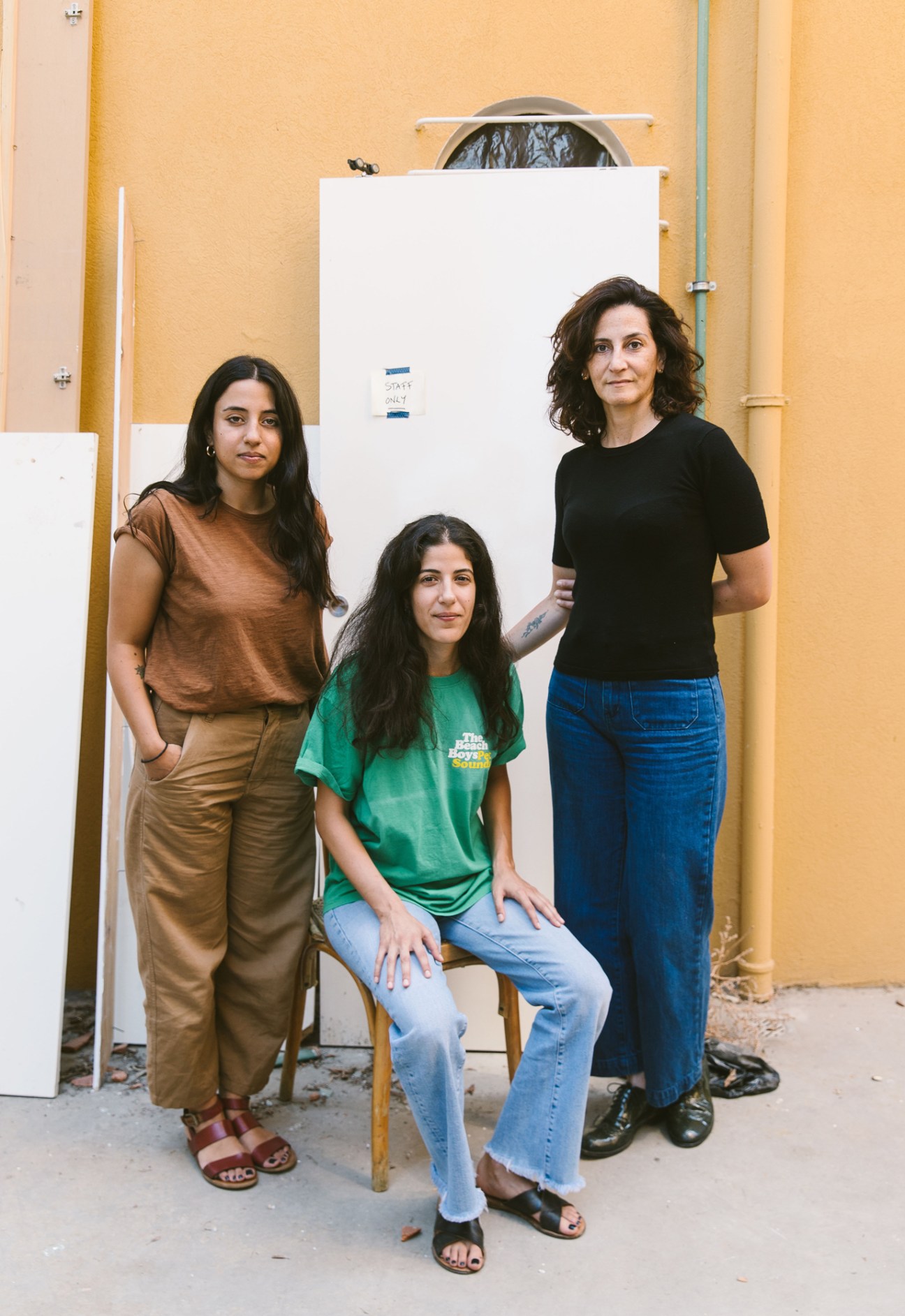 Three women from Papercup bookshop standing together outside, two standing and one sitting on a wooden stool