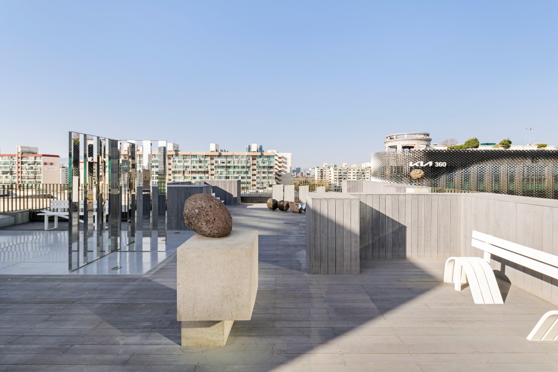 König gallery's rooftop sculpture garden with stone boulder sculpture, metal art installations, and Seoul cityscape.
