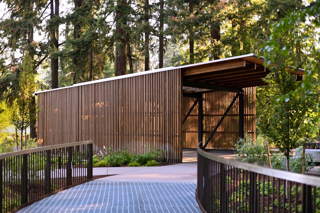 Elevated wooden walkway with metal grate decking weaving through tall forest trees at botanical gardens