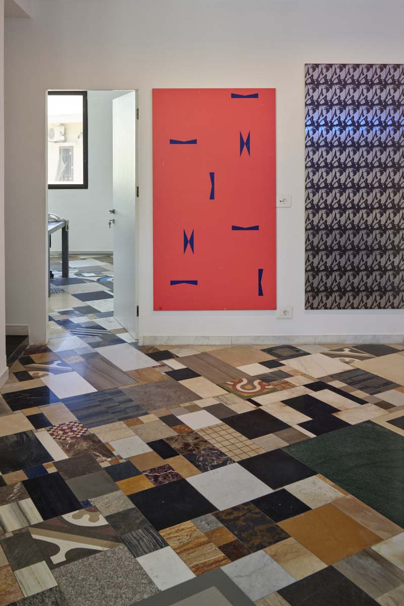Interior of Gregory Gatserelia's design studio showing patterned flooring, red artwork with blue marks, and decorative wall panels.