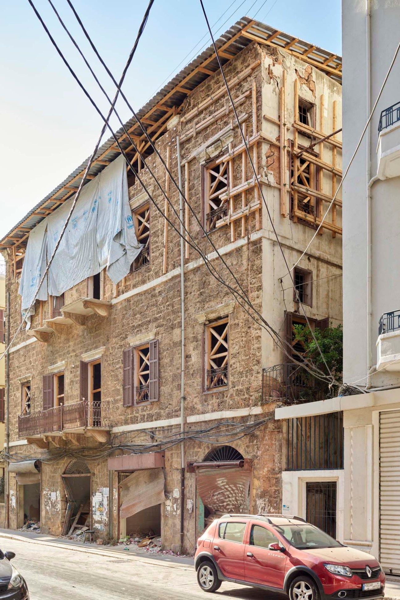 Damaged sandstone Liwan-style building with boarded windows and blast debris in Beirut.