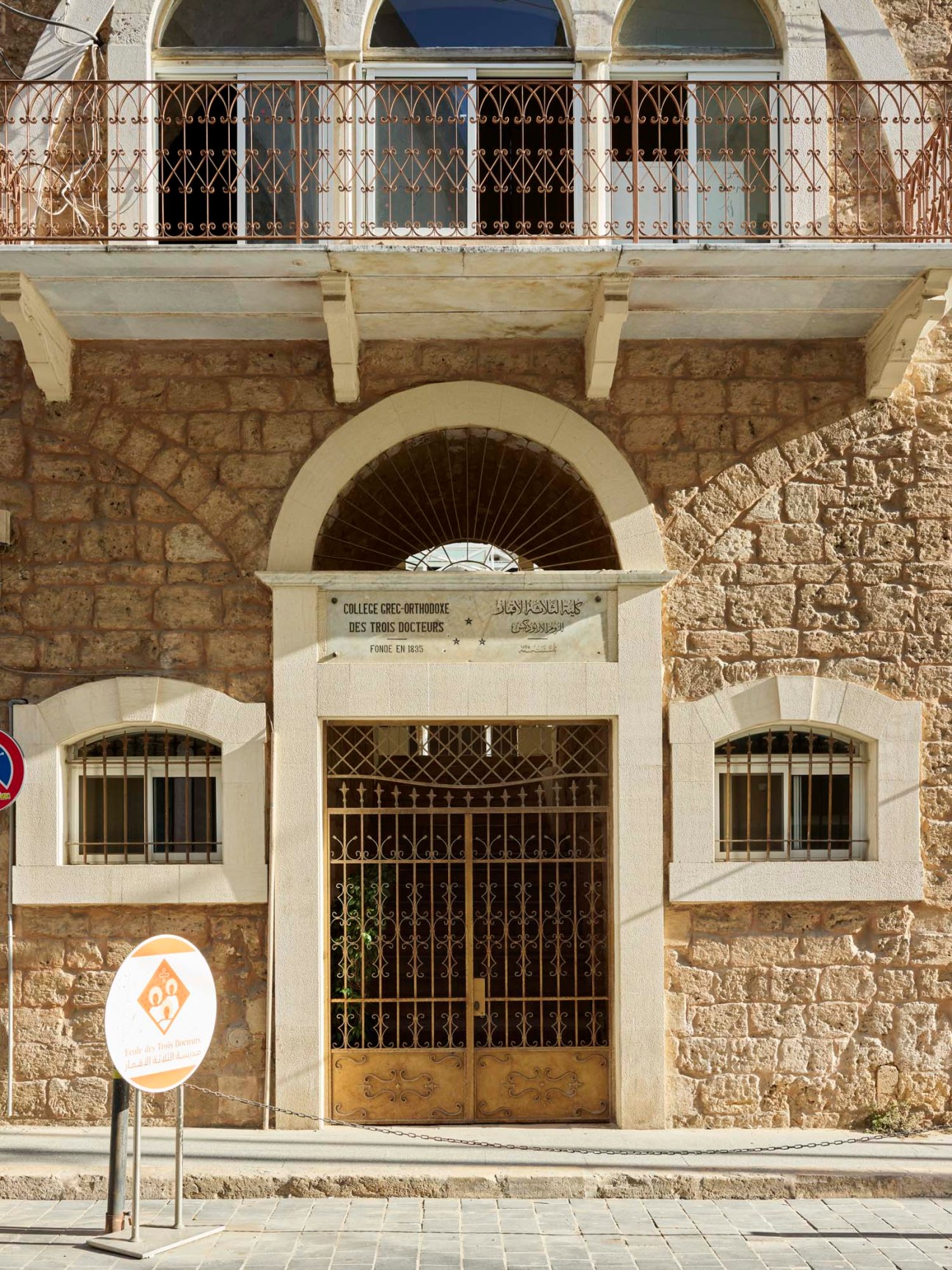 Traditional sandstone Liwan-style house in Beirut with high arched openings and ornate iron balcony railing.