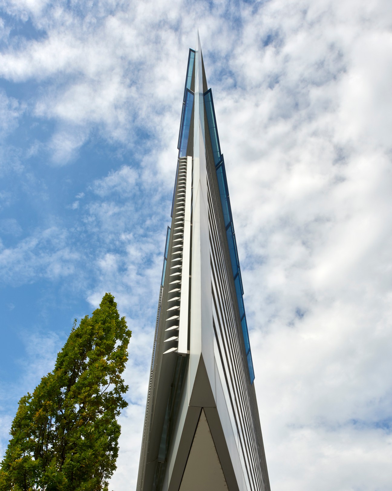 A tall concrete architectural spire with angular geometric forms pointing upward against a cloudy sky
