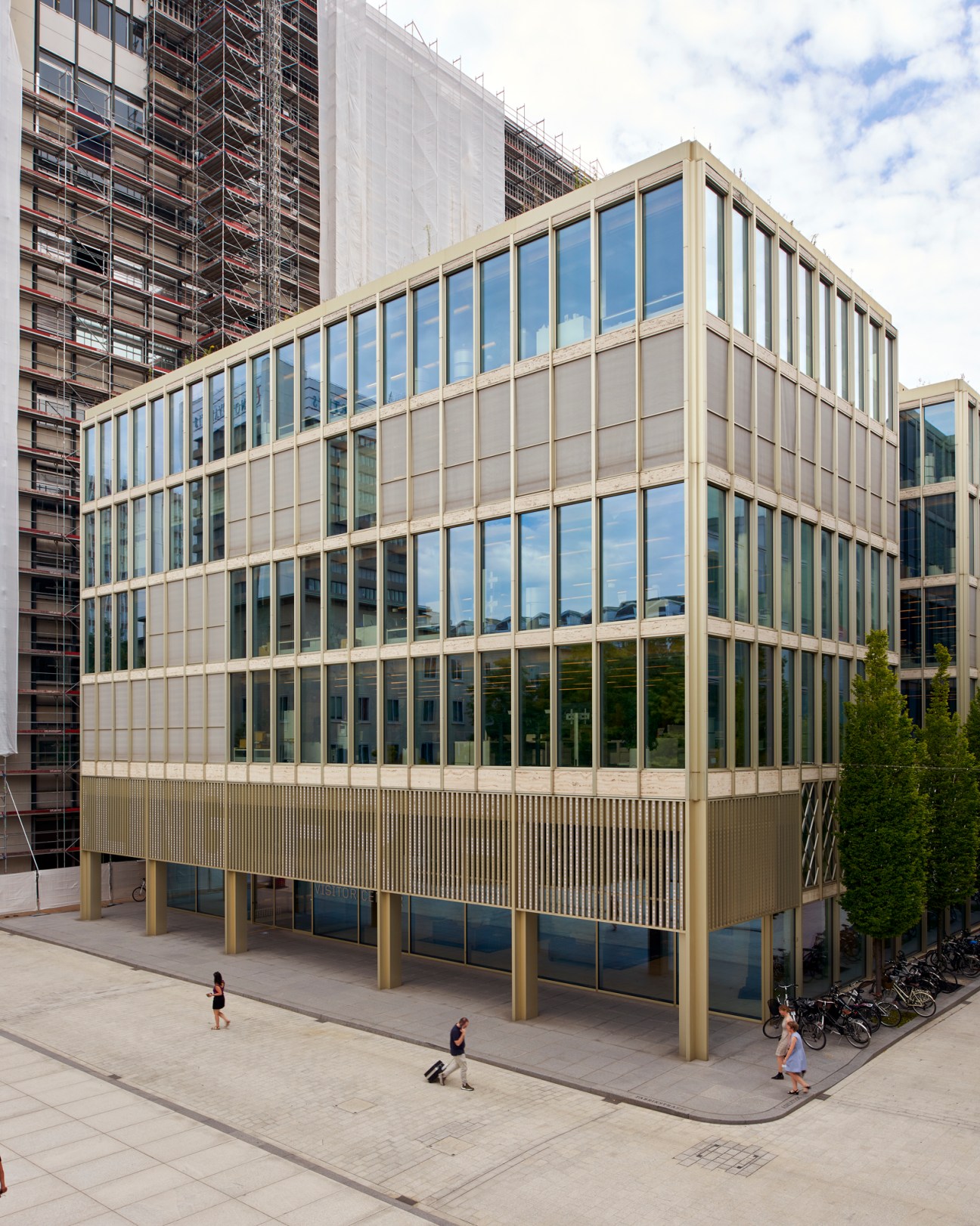 Modern glass office building with vertical facade elements elevated on pillars with people walking below