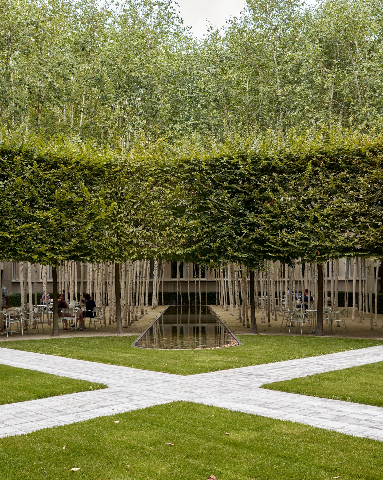 A landscaped courtyard with geometric water feature, planted trees in grid formation, and outdoor seating areas