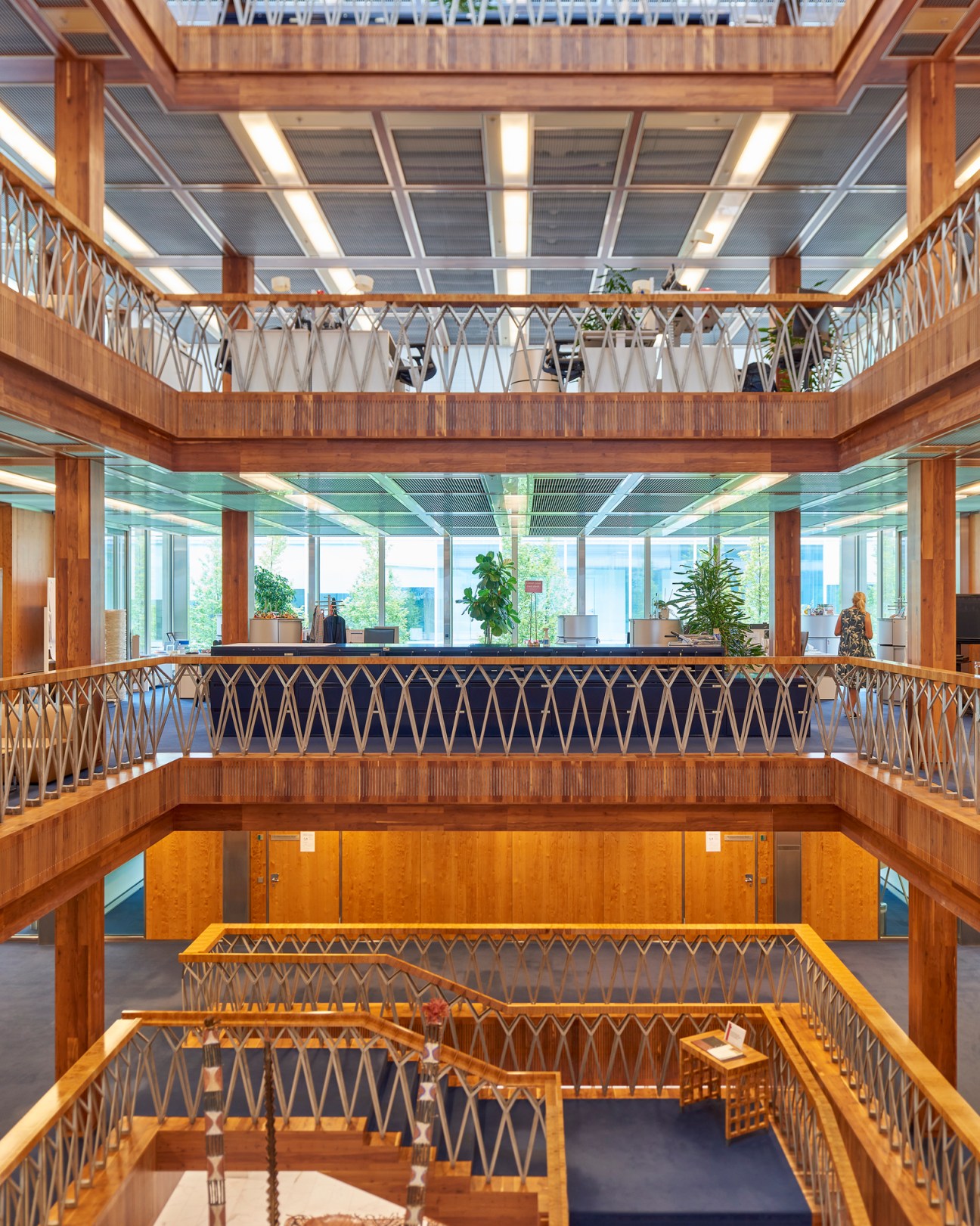 A multi-level atrium with wooden railings, geometric lattice details, and an open workspace visible on the upper floor
