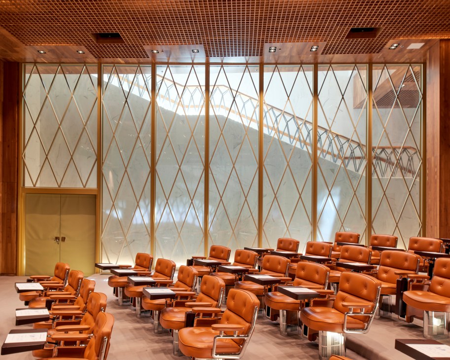 Modern auditorium with rows of orange leather chairs and large windows with geometric metal framework