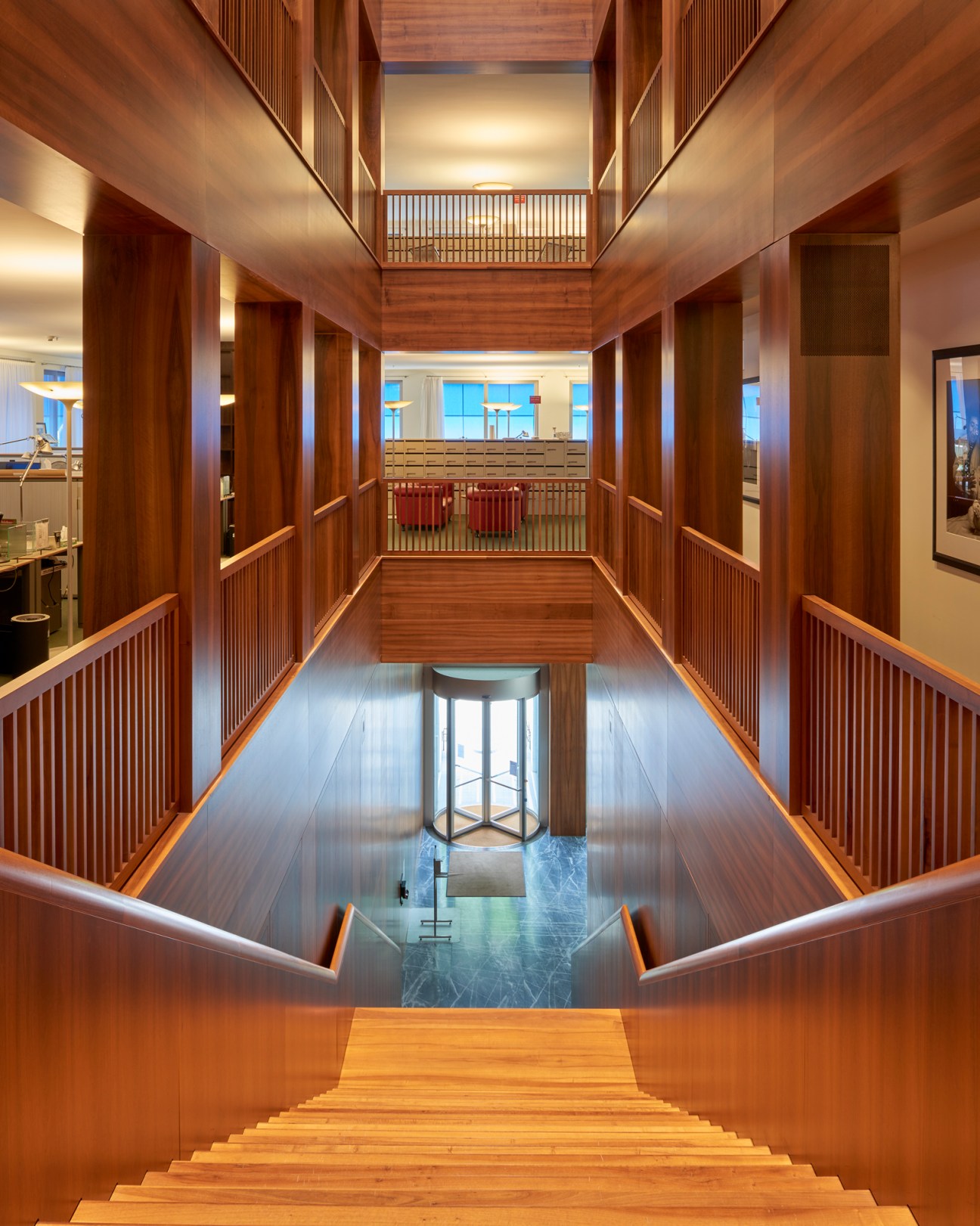 Multi-level wooden interior with vertical slat railings, warm lighting, and central staircase in modern building