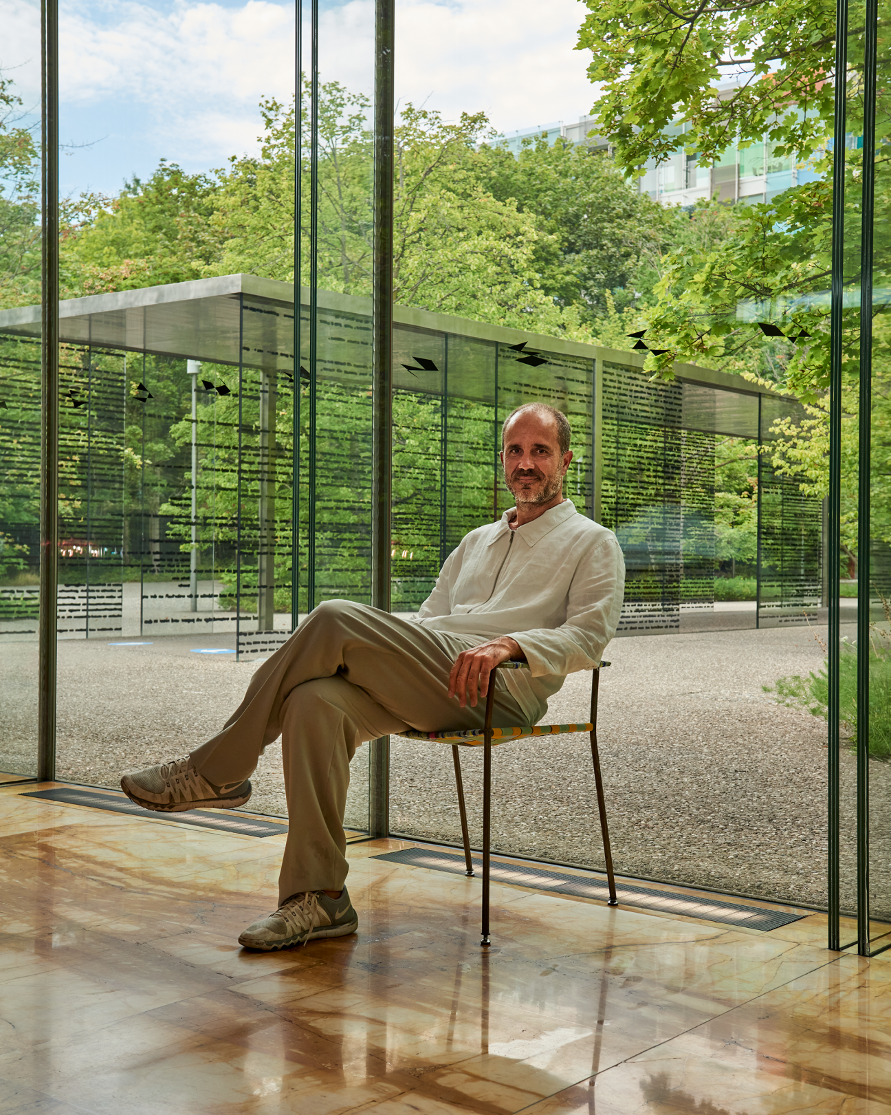 Marco Serra sitting on a chair in a modern glass-walled building interior with contemporary architecture
